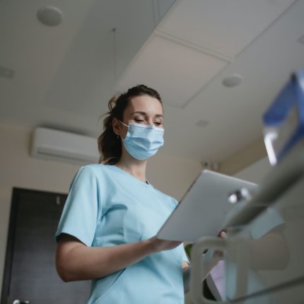 A nurse wearing a face mask looks at a tablet